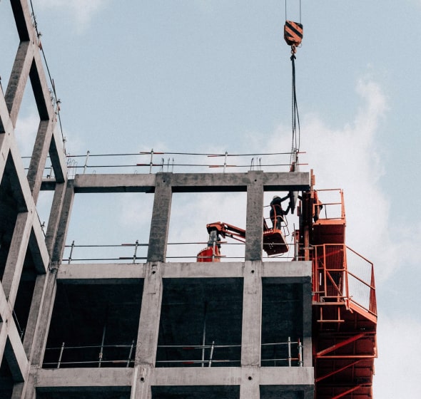À propos de nous 1 Des ouvriers du bâtiment, équipés de tenues de sécurité, manipulent du matériel et un crochet de grue sur la structure en béton d'un immeuble de grande hauteur.